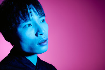 A stylish young man gazes into the distance, bathed in blue and pink lights.