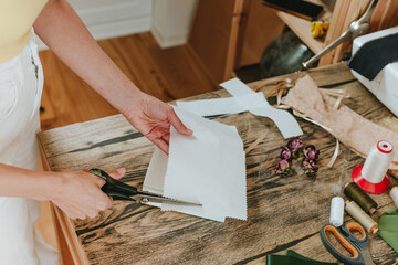 Close-up of woman cutting a decorative paper with scissors on wooden table indoor