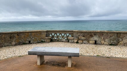 Oceanfront stone terrace with cloudy sky and empty bench, peaceful seaside retreat concept, ideal...