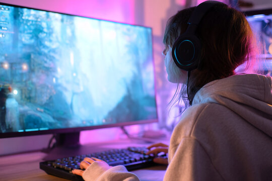 Gamer playing video game on large monitor, wearing headphones, illuminated by purple and blue light, showcasing intense gaming experience - Powered by Adobe