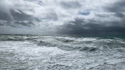 Dramatic stormy ocean waves beneath overcast sky, evoking concepts of nature's power and coastal...
