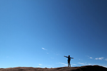 Silhouette of person with arms outstretched, standing on rock against clear blue sky, symbolizing freedom, achievement, and connection with nature