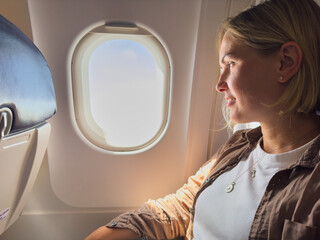 Passenger woman is flying in plane. Girl sitting in airplane looking out window going on trip...