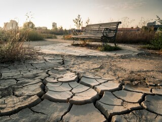 Park bench in a dry landscape shows signs of drought during sunset in urban area