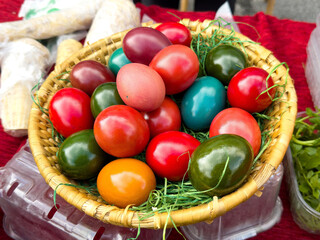 Colorful assorted eggs in woven basket on red fabric background