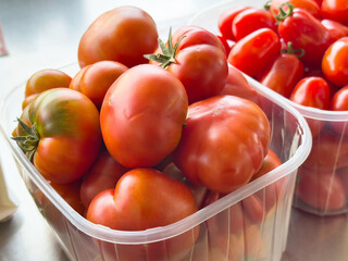 Fresh heirloom and roma tomatoes in plastic containers for kitchen use