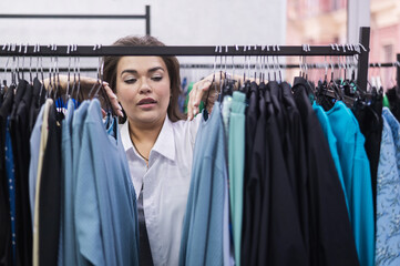 A smiling fat woman in a plus size store chooses clothes while sorting through the hangers. 