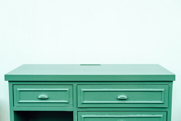 Green wooden table with drawers against a plain wall in a bright room setting