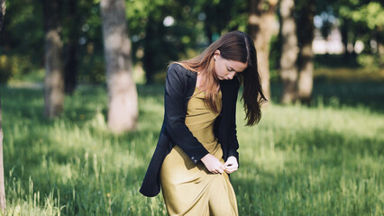 A young girl removes a speck of snot from her dress in the park.