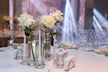Wedding table decor. Appliances, fresh flowers, candles in glass vases in close-up.