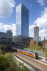 Fototapeta premium The picture features a dynamic train traveling through a densely populated urban landscape, set against a backdrop of towering skyscrapers, illustrating the lively atmosphere of London UK's cities