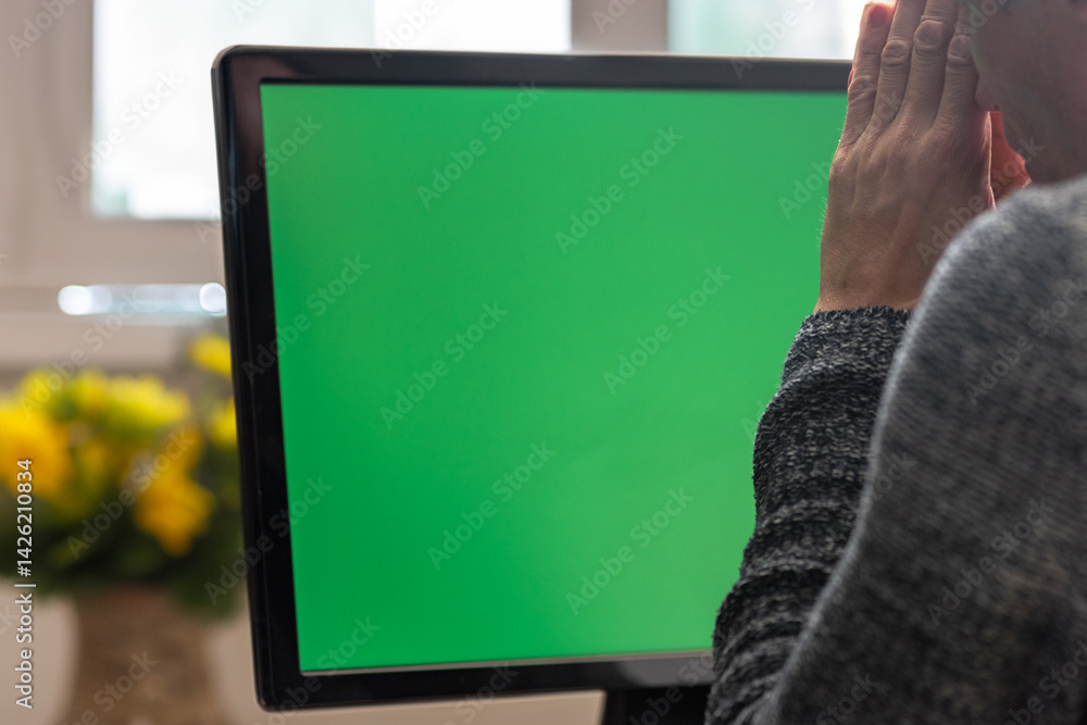 Poster Tired young man having problem and holding palms together while working on computer. A man in front of a monitor with chromakey, displaying visible emotions as he faces computer problems