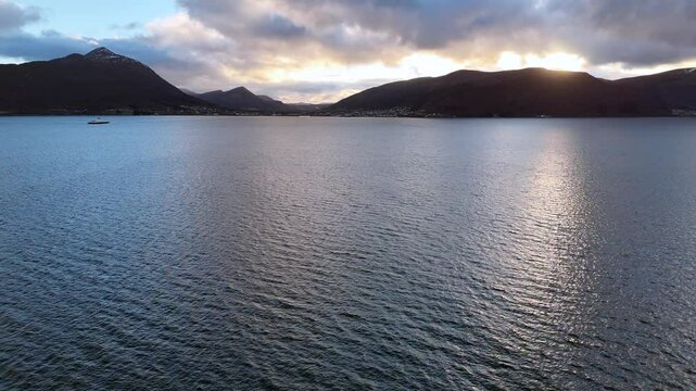 Drone view of the serene water of Sulafjorden with mountains and cloudy sunset sky in Norway.