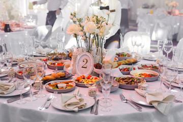 Table served for wedding banquet with cutlery and flowers in vases. Salads, appetizers and glasses.