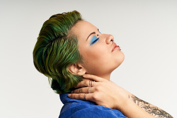 A young woman expresses her individuality with colorful hair and striking makeup, posing elegantly.