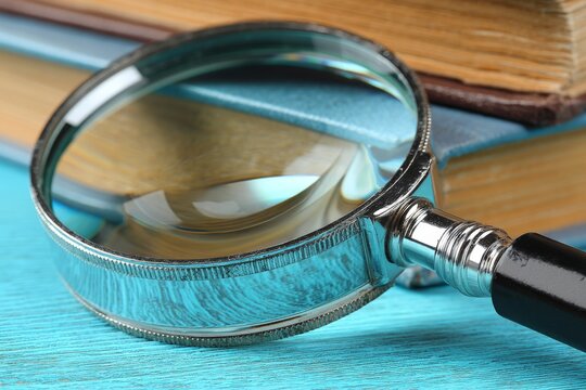 Close-up of a magnifying glass resting on stacked books on a wooden table
