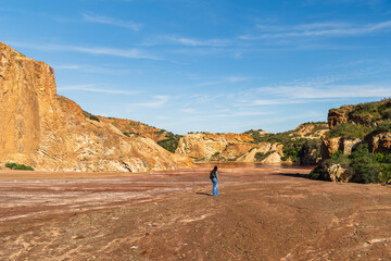 Person standing on barren mineral-stained terrain beneath ochre cliffs at the Mazarrón mines in...