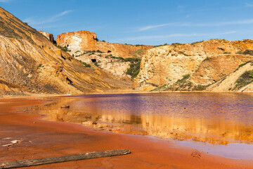 Toxic red lake reflecting orange cliffs in the abandoned Mazarrón mines, Murcia, Spain, showcasing mineral contamination, post-industrial decay, and surreal desert landscape
