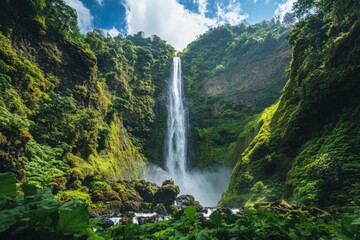 Fototapeta premium Majestic waterfall cascading down cliffs surrounded by lush green vegetation and bright blue sky