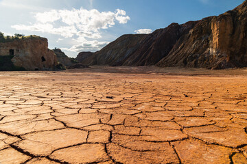 Cracked parched earth with oxidized mineral cliffs under blue sky at Mazarrón mines in Murcia, Spain, illustrating drought, environmental decay, and geological transformation