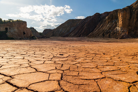 Cracked parched earth with oxidized mineral cliffs under blue sky at Mazarrón mines in Murcia, Spain, illustrating drought, environmental decay, and geological transformation