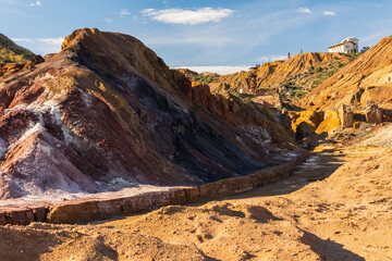 Color-rich oxidized slope and weathered ruins in Mazarrón mining landscape, Murcia, Spain, emphasizing geological layering, industrial history, and natural recovery