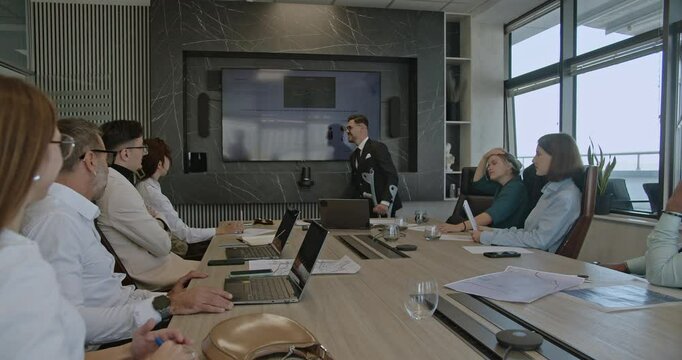 A businessman with crutches leads a presentation, demonstrating inclusivity and resilience in the workplace as he engages with his team.