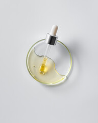 Glass dropper with yellow serum in transparent petri dish on white background