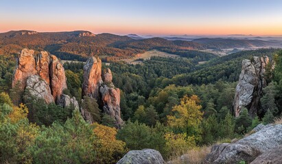 Fototapeta premium Panoramic sunrise view over a vast, forested landscape with towering rock formations. Autumnal colors paint the trees