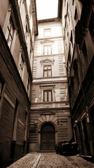 Fototapeta premium Sepia-toned alleyway in European city, old buildings, cobblestone street, car parked, possible tourism photo