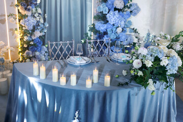 Wedding table for the bride and groom is decorated with a tablecloth, flowers and candles in blue.