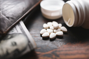 White medicine pills, medication, treatment with US dollar banknotes and wallet, close-up view