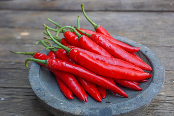 Fresh red chili peppers arranged on a rustic stone plate over a wooden table, showcasing vibrant color and natural texture.