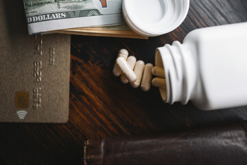 White medicine capsules and medication pills with US dollar banknotes, credit card and wallet, top view