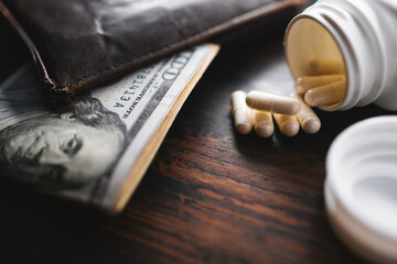 White medicine capsules and medication pills with US dollar banknotes and wallet, close-up view