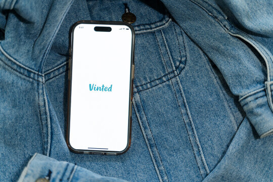 Iphone with vinted logo on screen on vintage denim fabric. Vinted is a Lithuanian online marketplace and community for second hand clothes and accessories.