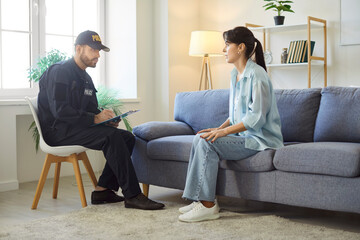 Concentrated male police officer or detective investigates a crime, interviewing a victimized woman about burglary and theft at home living room. Law enforcement in solving crimes.