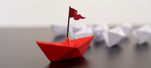 Red origami boat with a small flag positioned on the right against a clean white background.