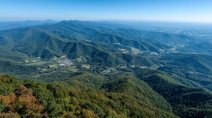 Naklejka premium Panoramic view of a vast mountain range, lush green valleys, and distant cityscape under a clear blue sky.