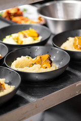 A close-up of dark bowls filled with creamy mashed potatoes topped with savory meat and melted cheese, arranged on a kitchen counter, showcasing a delicious and appealing meal.