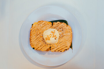 Flat lay of caramel sauce toast bread and vanilla ice cream with sprinkled nuts topping on white plate