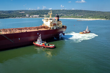 A large cargo ship assisted by two tugboats in a harbor. The vessels maneuver through deep blue...