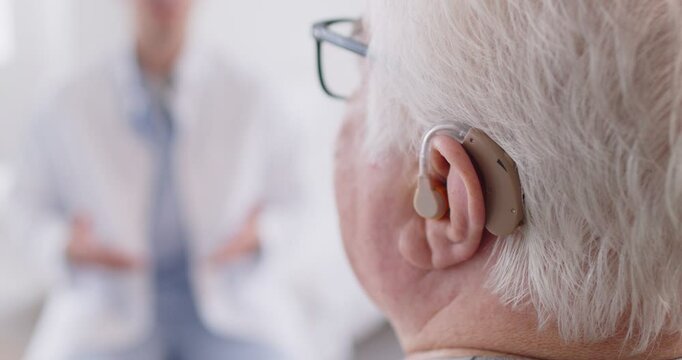 Close up back view of senior man wearing hearing aid having consultation with male audiologist or otolaryngologist. Elderly deaf man with plastic hearing device, having hearing loss and ear problems.