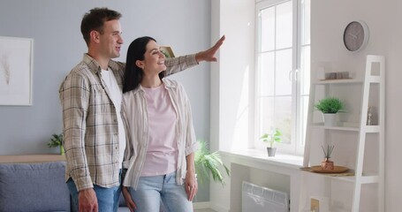 Happy couple standing in modern room at home, smiling wife and husband excited by relocation, satisfied clients purchased new apartment, mortgage, planning rennovation, wall inspirational design
