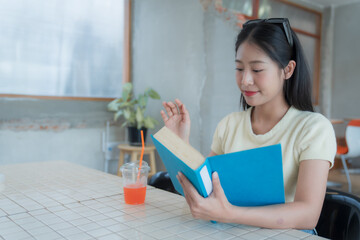 Concentrating on a book while sipping refreshing juice, a young Asian woman enjoys her leisure time...