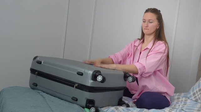 Woman closing overpacked suitcase on bed