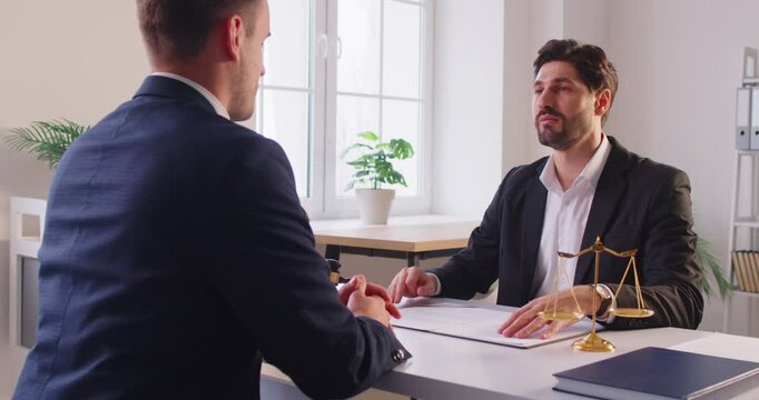 Attorney or lawyer and client discussing a case and reviewing paperwork during a meeting in the office. Negotiating contracts, examining legal details, and collaborating on important legal matters.