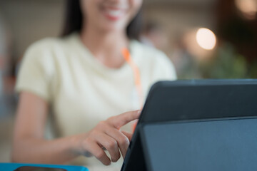 Young woman smiling while using a tablet, touching the screen with her finger. Dressed in a light t-shirt, sitting comfortably in a cafe with a blurred background