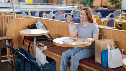 Caucasian woman having lunch in a cafe with her Jack Russell terrier dog in a stroller. 