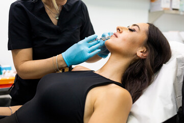 An unrecognizable aesthetic doctor injects hyaluronic acid into a girl's lips in a modern clinic. Concept of hyaluronic acid on lips, aesthetic operations on lips.